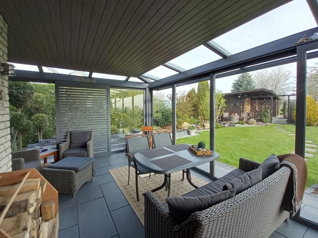 Moderner Wintergarten aus Aluminium und Glas an einem Einfamilienhaus mit rotem Ziegeldach und angrenzender Terrasse