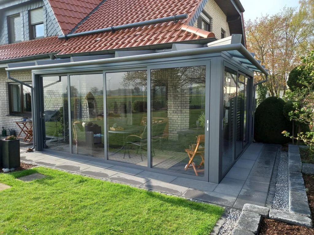 Moderner Wintergarten aus Aluminium und Glas an einem Einfamilienhaus mit rotem Ziegeldach und angrenzender Terrasse