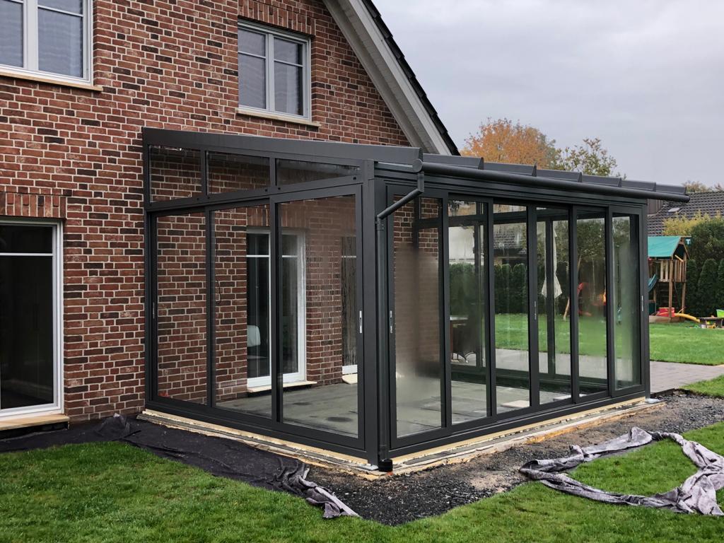 Kalter Wintergarten mit Aluminium-Glaskonstruktion an einem Backsteinhaus, geeignet als Wetterschutz, Pflanzenraum oder überdachte Terrasse.
