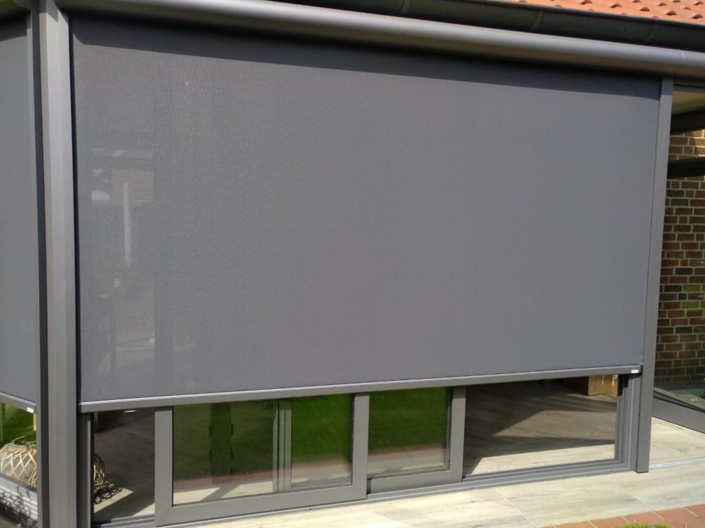 Senkrechter Textilscreen als Sonnenschutz an einem modernen Wintergarten mit bodentiefen Glasflächen.