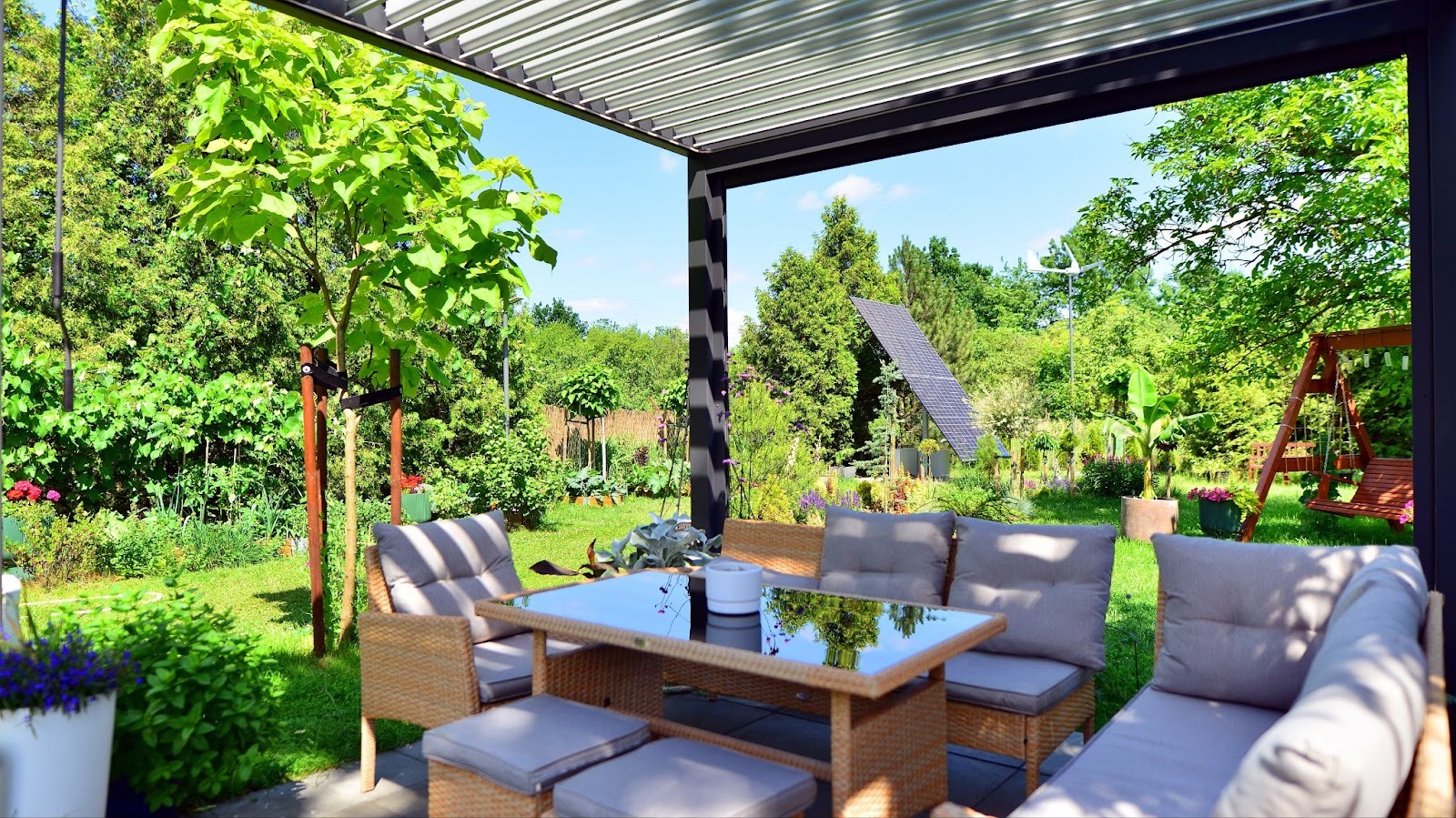 Moderne Terrasse mit Lounge-Möbeln, umgeben von einem gepflegten Garten bei Sonnenschein.
