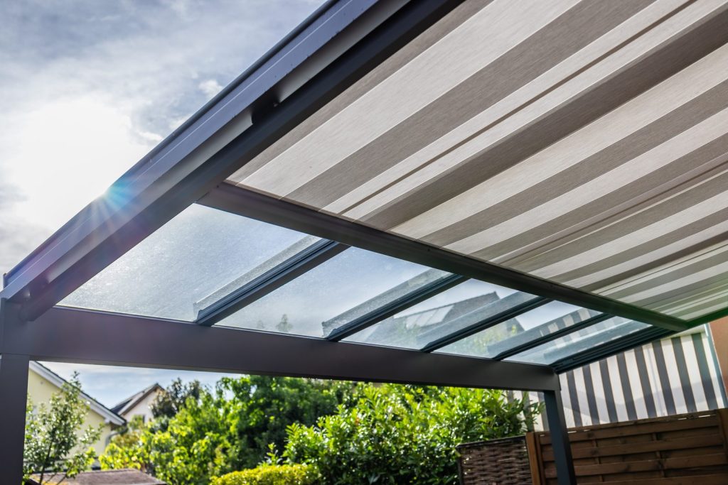 Glasüberdachung mit schwarzem Metallrahmen und transparenten Glasscheiben unter bewölktem Himmel