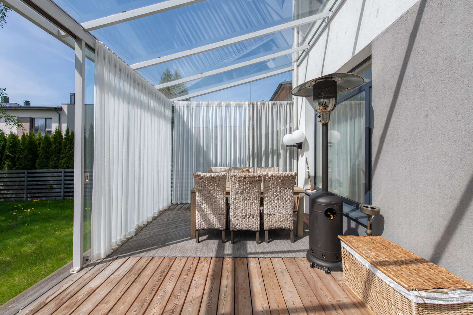 Terrasse mit Glasdach, Sitzbereich mit sechs Stühlen und einem Heizstrahler neben einem modernen grauen Haus